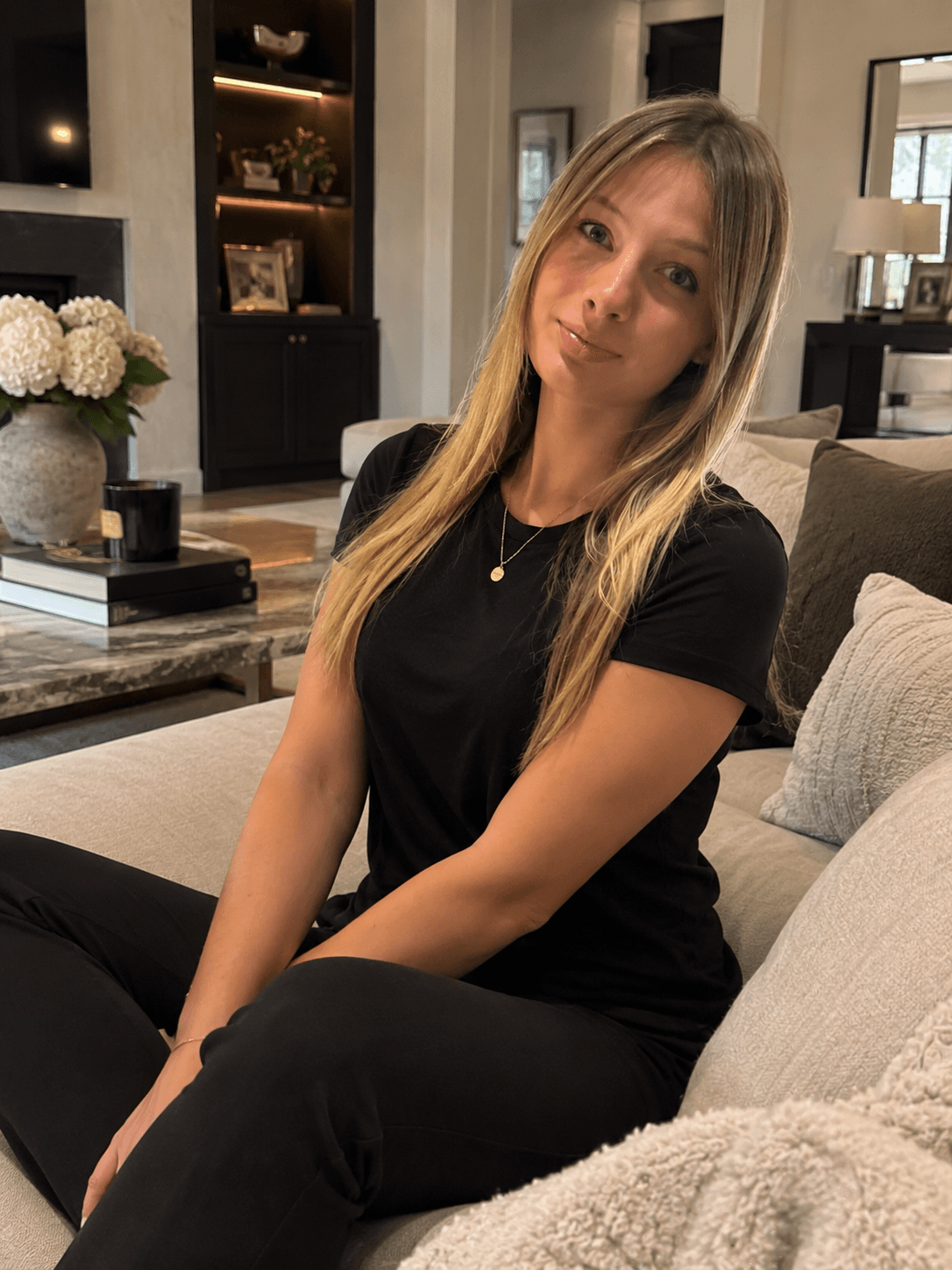 Blonde woman in black t-shirt sits on a beige sofa in a stylish living room.